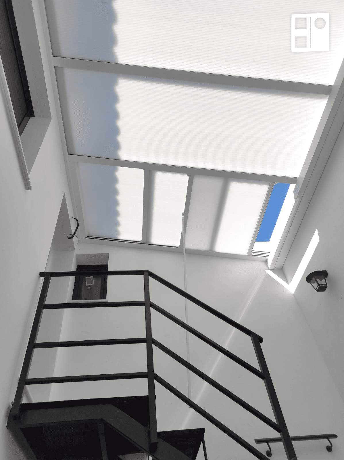 Escalera de hierro negro con barandillas bajo un tragaluz en un espacio interior luminoso.