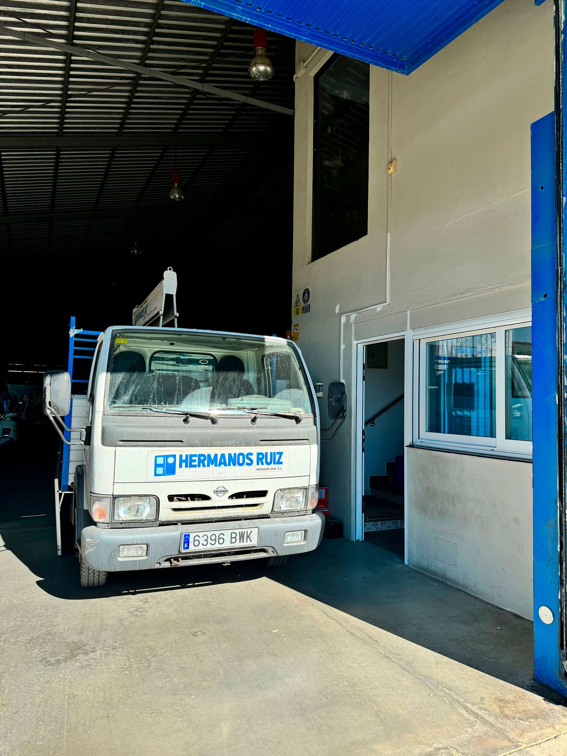 Camión de la empresa Hermanos Ruiz aparcado en la entrada de un taller con puertas azules.
