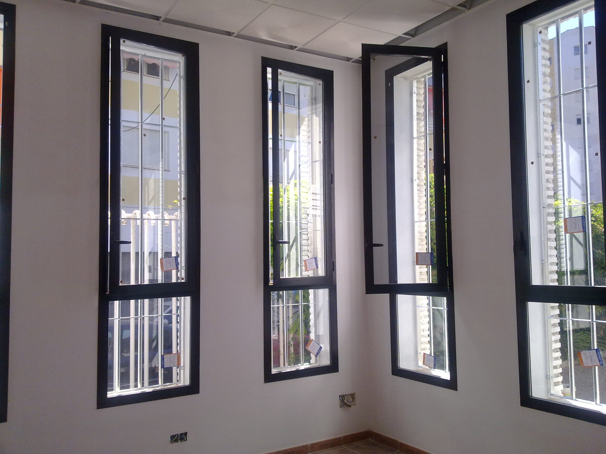 Interior de una habitación con ventanas de aluminio abiertas hacia el exterior.